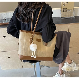 Detail of a large beige wavy fabric tote bag with brown leather trim and a plush charm