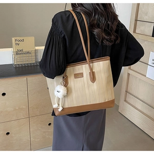 Detail of contrast stitching on beige canvas tote bag with brown leather handles and plush charm