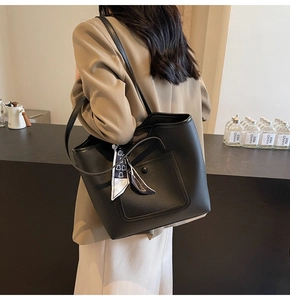 Detail of black pebbled leather tote bag featuring a decorative geometric silk scarf handle