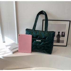 Deep green quilted tote bag shown next to a tablet for size reference in a bright room