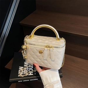 Quilted beige bucket bag with gold handle and chain strap shown in a lifestyle setting