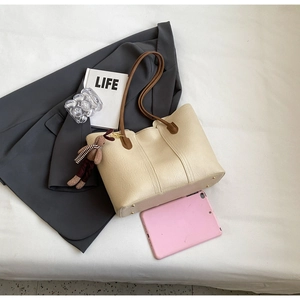 Detail view of cream tote bag with brown straps and rabbit charm on a gray blazer