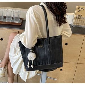 Detail of black faux leather tote with vertical rippled texture and fuzzy charm