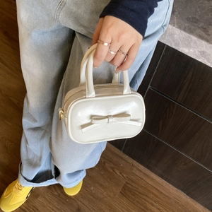 Detail view of mini white patent leather handbag featuring a bow and metal zipper closure
