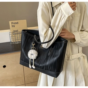 Close-up of black textured tote bag featuring fashion leather tag and a plush toy charm