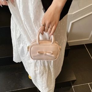 Detail of light pink mini bag featuring a glossy bow and golden D-ring hardware