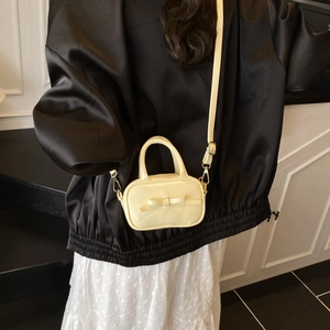 Detail of a beige mini crossbody bag for kids featuring a bow and adjustable strap