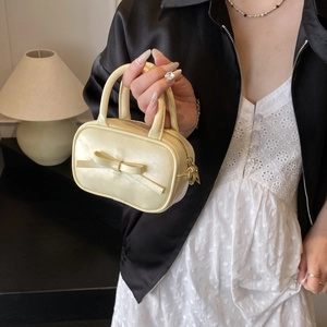 Detail of cream mini handbag featuring a bow decoration and smooth leather texture