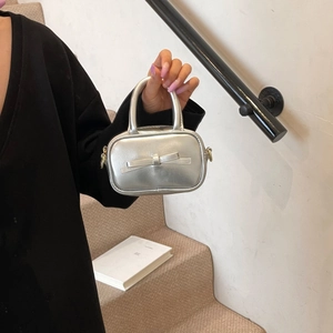 Silver mini bow handbag with metallic finish shown in a hand-held lifestyle close-up shot