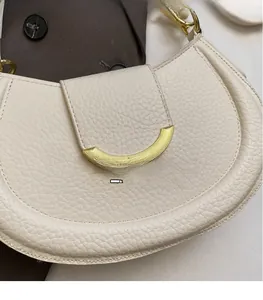 Detail of cream lychee texture leather saddle bag featuring a gold crescent metal clasp