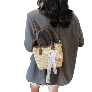 Straw bucket bag with leather handles and white lace bow on a female model