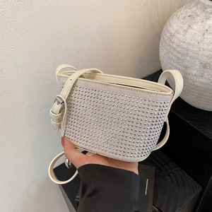Close-up of cream underarm bag featuring silver rivets and adjustable leather strap