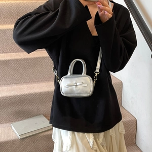 Silver mini leather handbag with bow detail worn as a crossbody bag in lifestyle setting