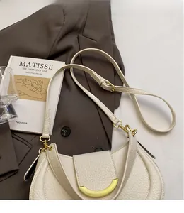 Detailed close-up of cream pebble leather saddle bag with golden crescent metal buckle