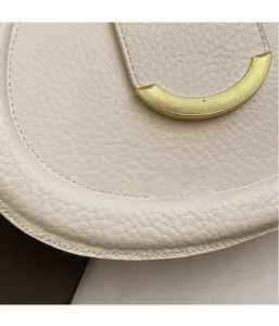 Detailed macro view of white lychee texture leather saddle bag with golden metal buckle