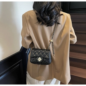 Detail of black quilted leather shoulder bag with gold clover clasp and metal chain strap
