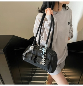 Detail of black faux leather Boston bag with front pockets and silver heart chain