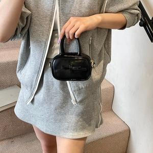 Close-up of a mini black bow handbag held by a model in casual grey loungewear