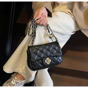 Close-up of black quilted leather bag with gold chain strap and clover twist lock