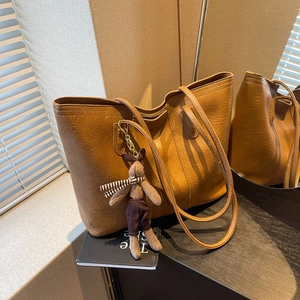 Brown vintage leather tote bag with plush rabbit charm on a dark vanity table