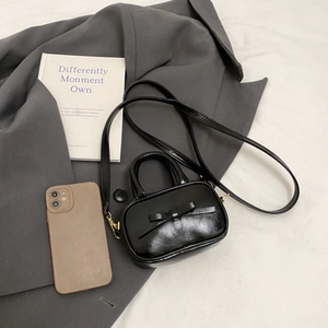 Detail of a mini black bow handbag on a grey blazer with fashion accessories
