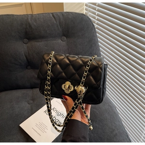 Close-up of black quilted leather bag with gold clover lock and adjustable chain strap