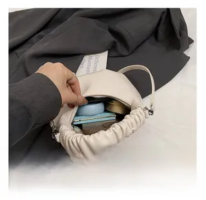 Detail view of cream-white crossbody bag interior capacity with pleated handle