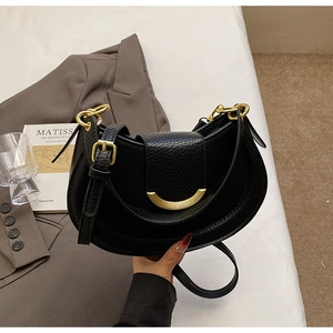 Detail of black lychee grain leather saddle bag with golden hardware in urban setting