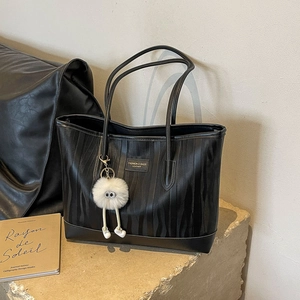Black animal texture leather tote bag with plush charm on stone base for commuting