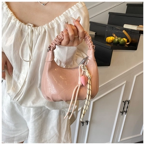 Close-up of pink PU leather handbag featuring a ruched handle and heart pendant charm