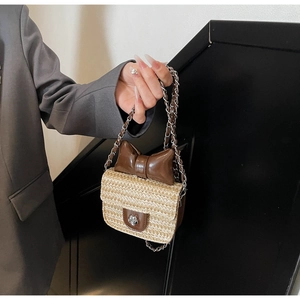 Détail d'un petit sac bandoulière en paille avec nœud en cuir marron et chaîne métal