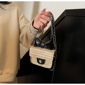 Détail du mini sac en paille avec nœud noir, chaîne en métal et fermoir fleuri