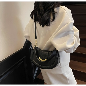 Detail of black lychee grain leather crossbody bag with golden half-moon hardware