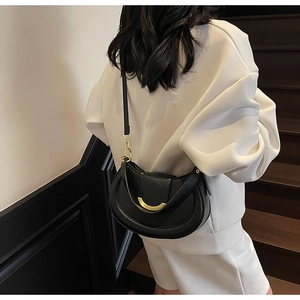 Detail of black pebbled leather half-moon bag with gold metal clasp on white tracksuit