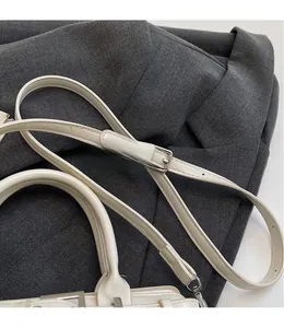Close-up of cream white leather strap with silver adjustable buckle on a crossbody bag