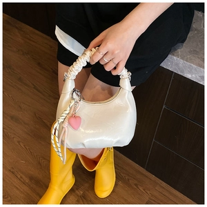 Close-up of white glossy crossbody bag with stylish pleated handle and heart charm detail