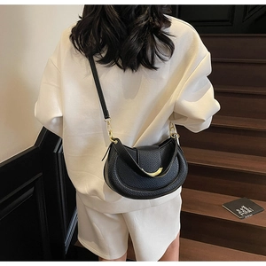Detail shot of a black pebble leather half-moon bag on a model with white clothes