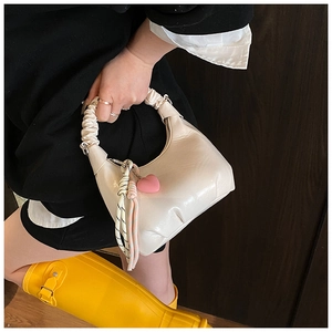 Detail of cream half-moon bag featuring ruched handle and pink heart charm with scarf