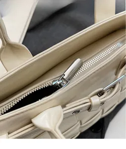 Detailed macro view of the smooth metal zipper head on a woven cream bucket bag