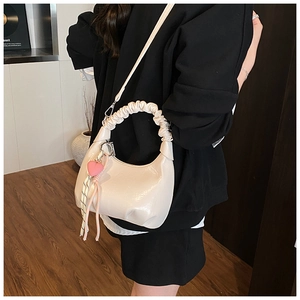 Detail of a creamy beige crescent bag with ruffled handle and heart pendant accessory