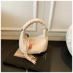 Detail of cream white pleated hobo bag with pink heart pendant and woven strap