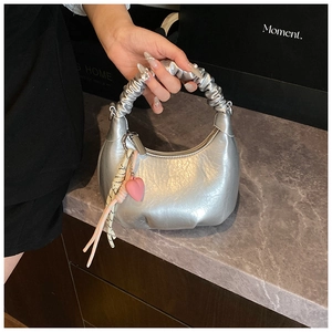 Detail of silver metallic hobo bag featuring gathered handles and pink heart charm