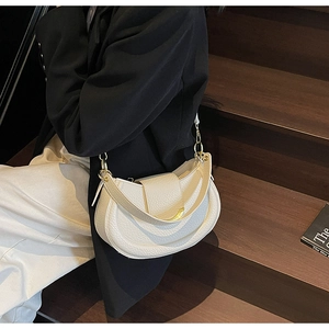 Detail of white pebbled leather crescent bag with curved gold clasp worn on shoulder
