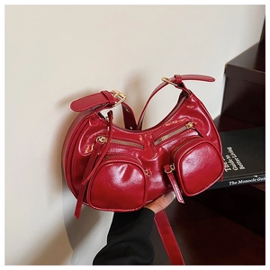 Detail of red crescent moon shoulder bag featuring dual zipper pockets and gold hardware