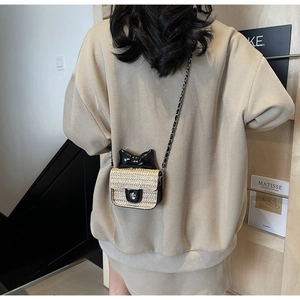 Détail d'un mini sac bandoulière en paille avec un nœud noir et une bandoulière en chaîne