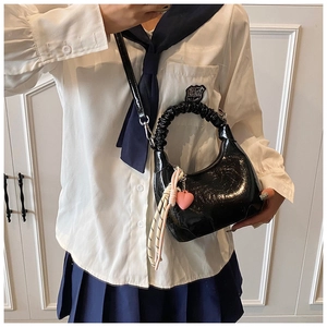 Detail of black glossy patent leather hobo bag with pink heart charm and pleated handle