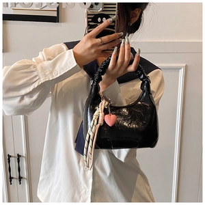 Detail of glossy black patent leather handbag featuring pleated handle and heart charm
