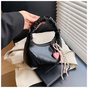 Close-up of black glossy faux leather handbag with cloud pleated handle and pink heart charm