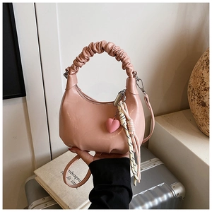 Pink crescent bag with cloud-like gathered handle and heart charm on a vintage suitcase