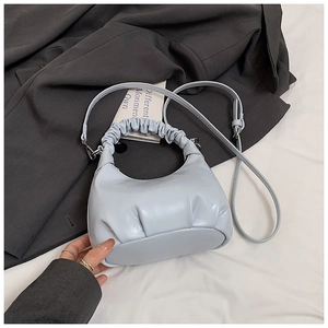 Detail view of a light blue crescent bag with pleated handles on a suit background